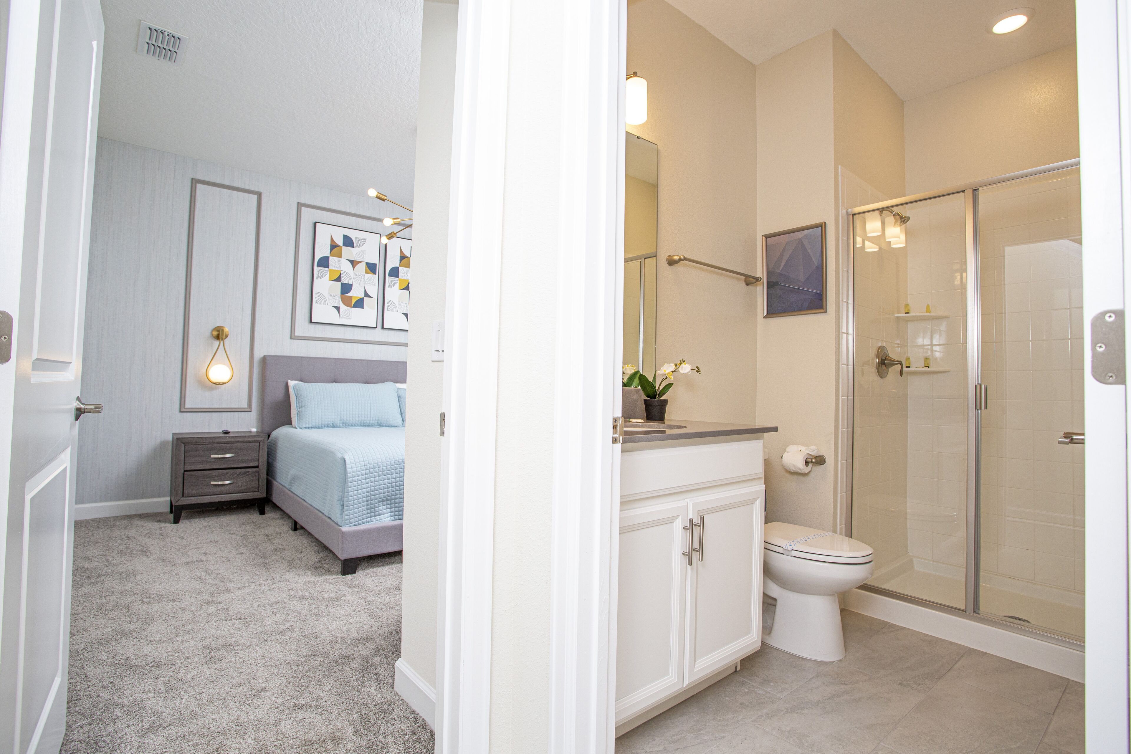 A bedroom with a bed, nightstand, and wall art. The bathroom has a toilet, sink, and shower.