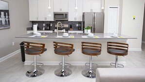 Una cocina moderna con armarios blancos, electrodomésticos de acero inoxidable y una isla central con taburetes de bar.