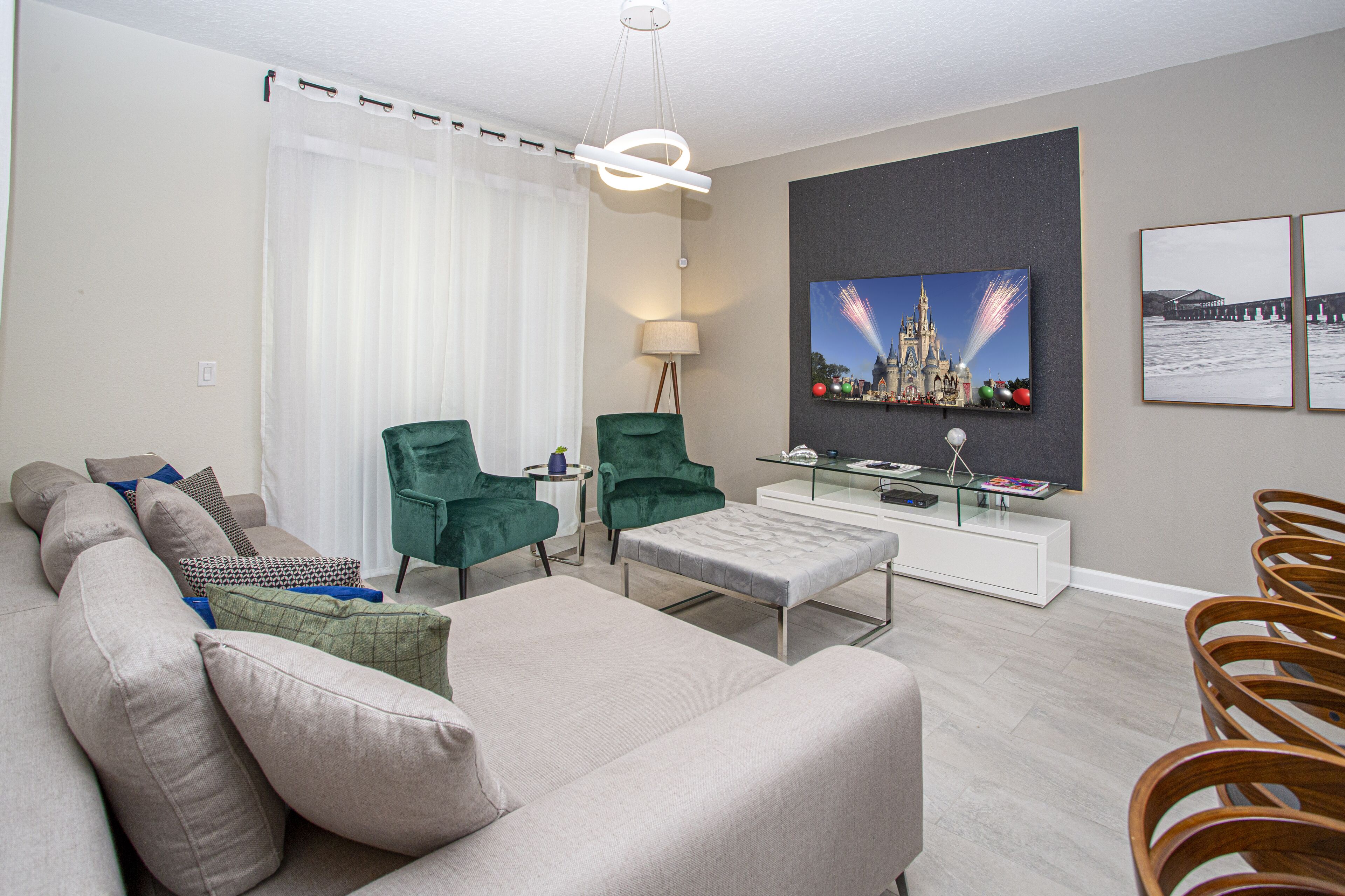 Een moderne woonkamer met een bank, twee groene fauteuils, een glazen salontafel en een flatscreen televisie aan de muur.