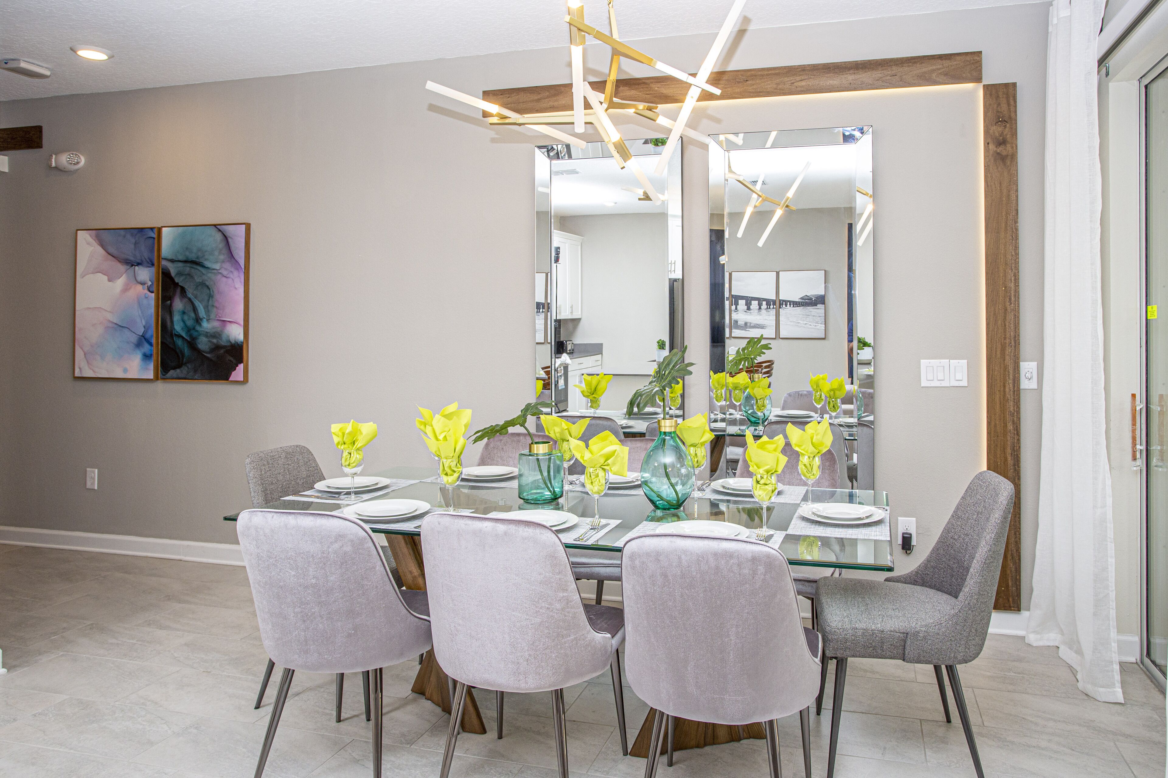 Un comedor moderno con una mesa de vidrio, sillas tapizadas en gris y flores amarillas.