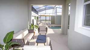 Un patio soleado con piscina, sillas de descanso y una mesa.