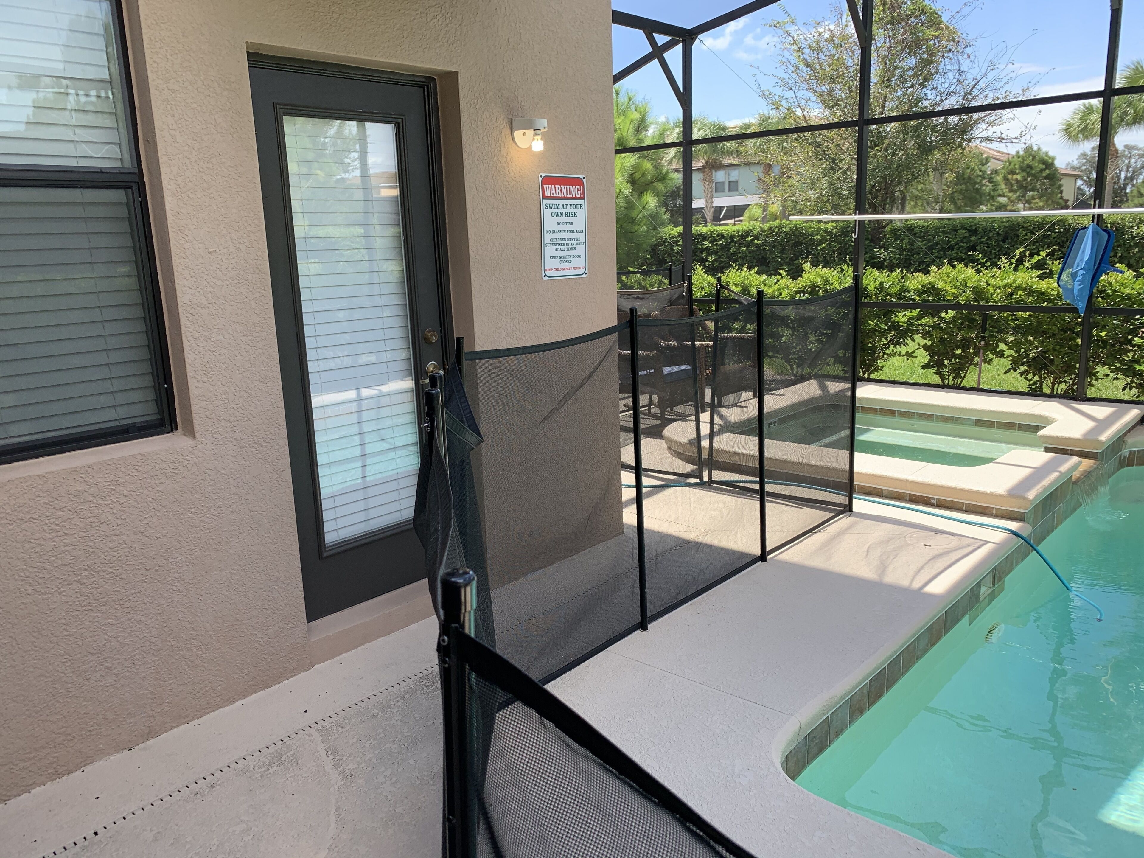 A pool area with a glass enclosure, a door with a sign, and a view of a residential neighborhood.
