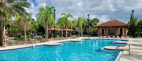 A swimming pool with lounge chairs and umbrellas, surrounded by palm trees and a building labeled "Restrooms".