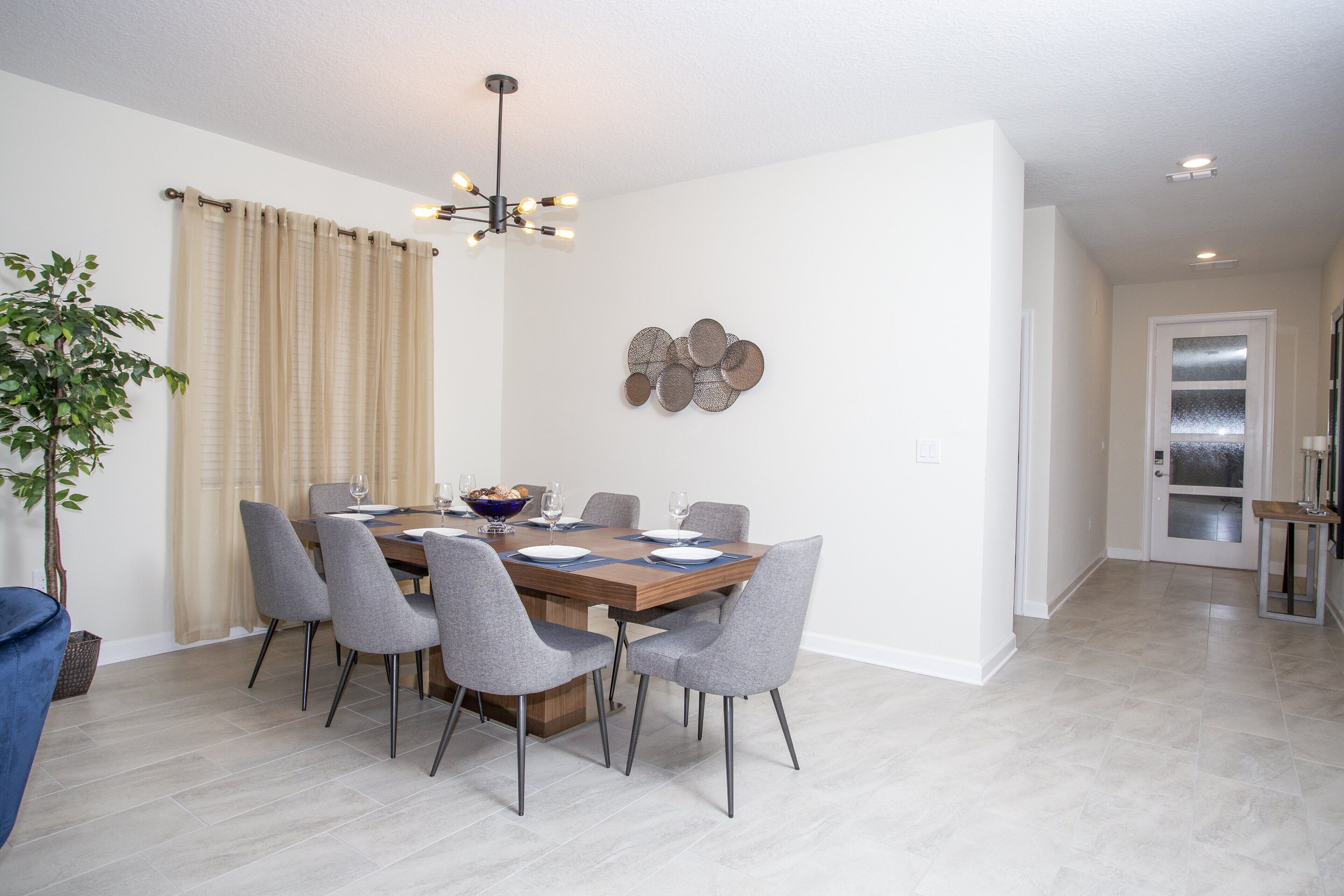 A dining area with a wooden table, grey chairs, and a chandelier.
