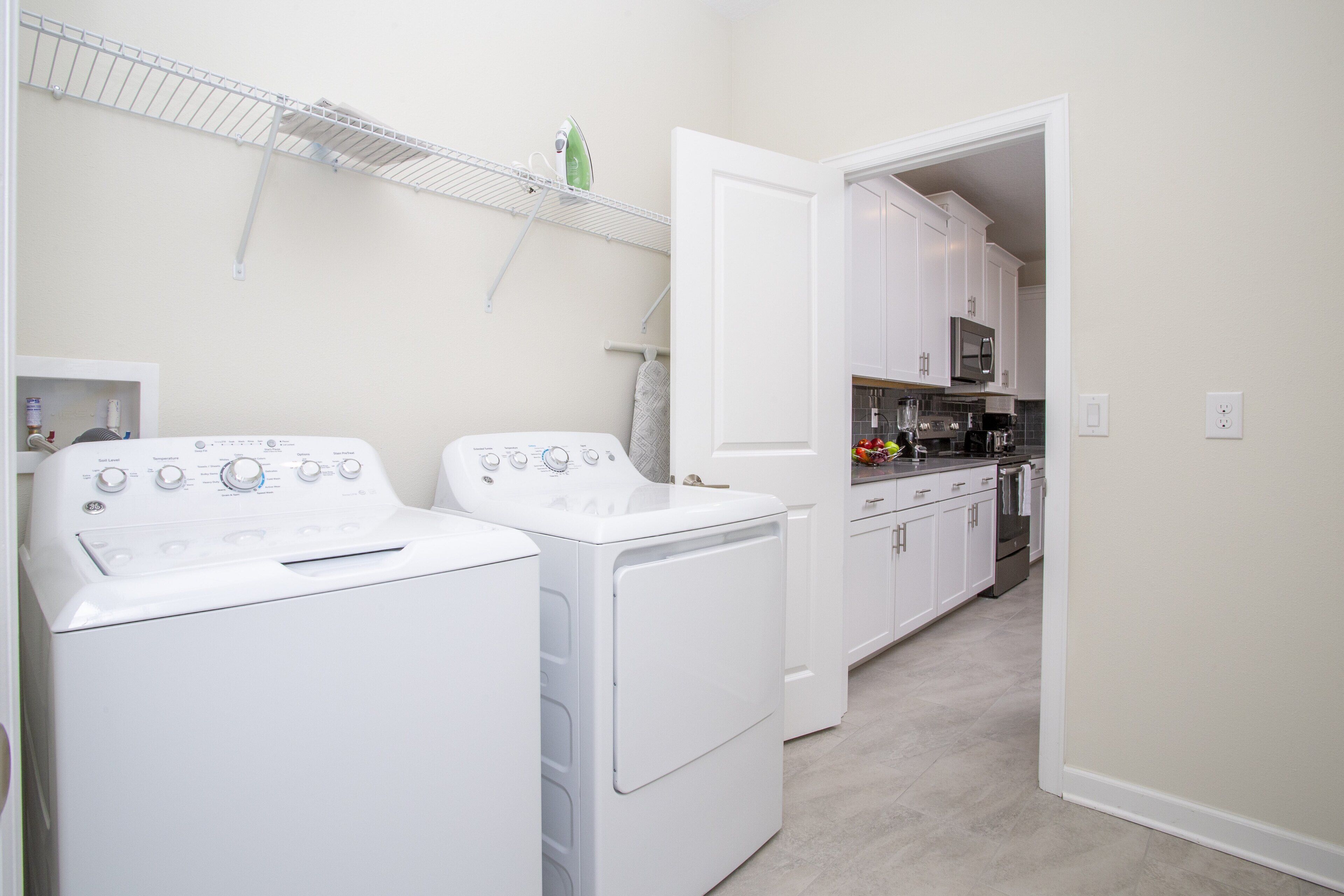Un'area lavanderia con due lavatrici bianche, un forno a microonde e una cucina con mobili bianchi.