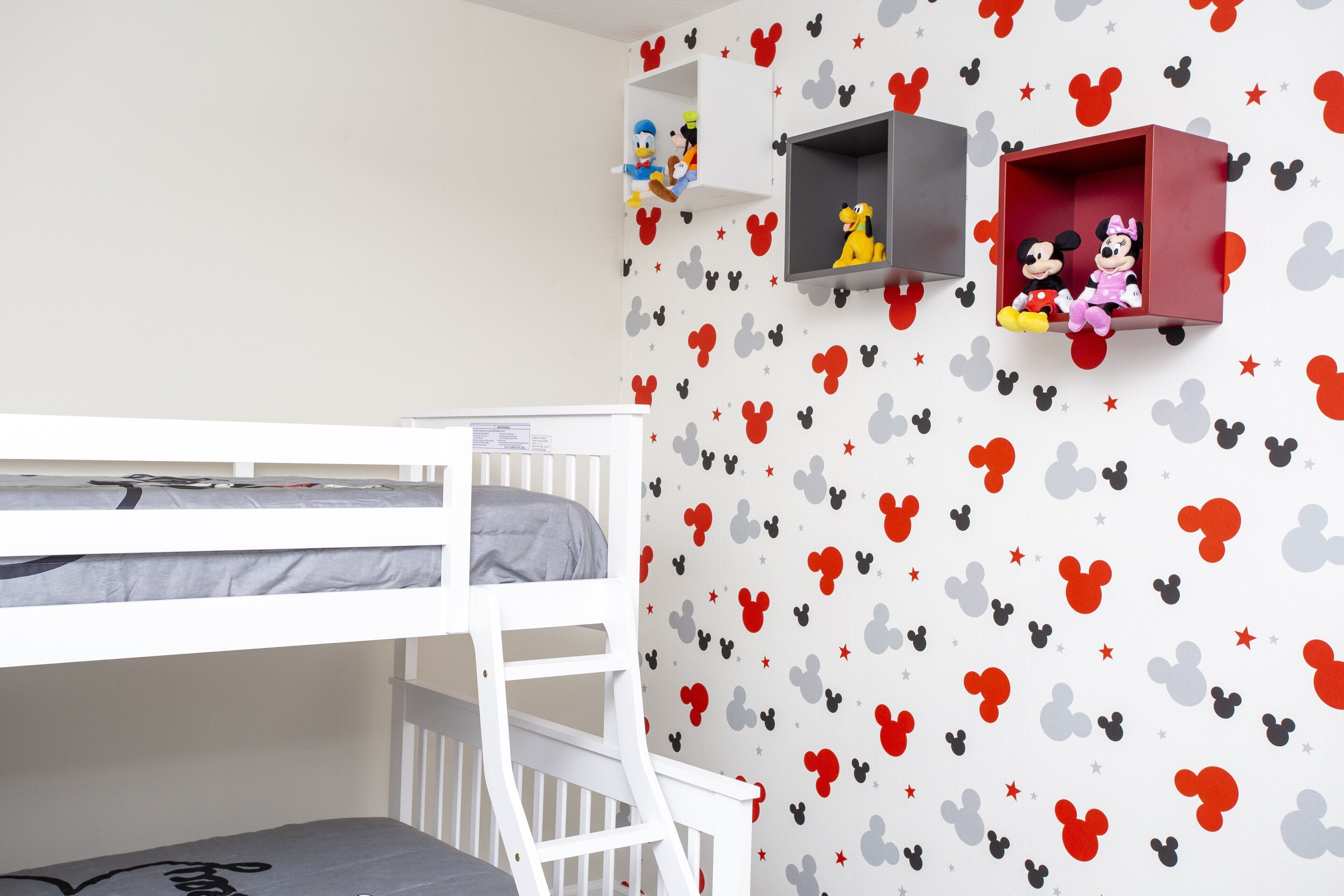 Une chambre d’enfant avec un lit superposé, des autocollants de Mickey Mouse sur les murs et des étagères remplies de jouets.