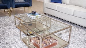 Ein Wohnzimmer mit einem Glastisch, einem weißen Sofa und zwei blauen Sesseln.