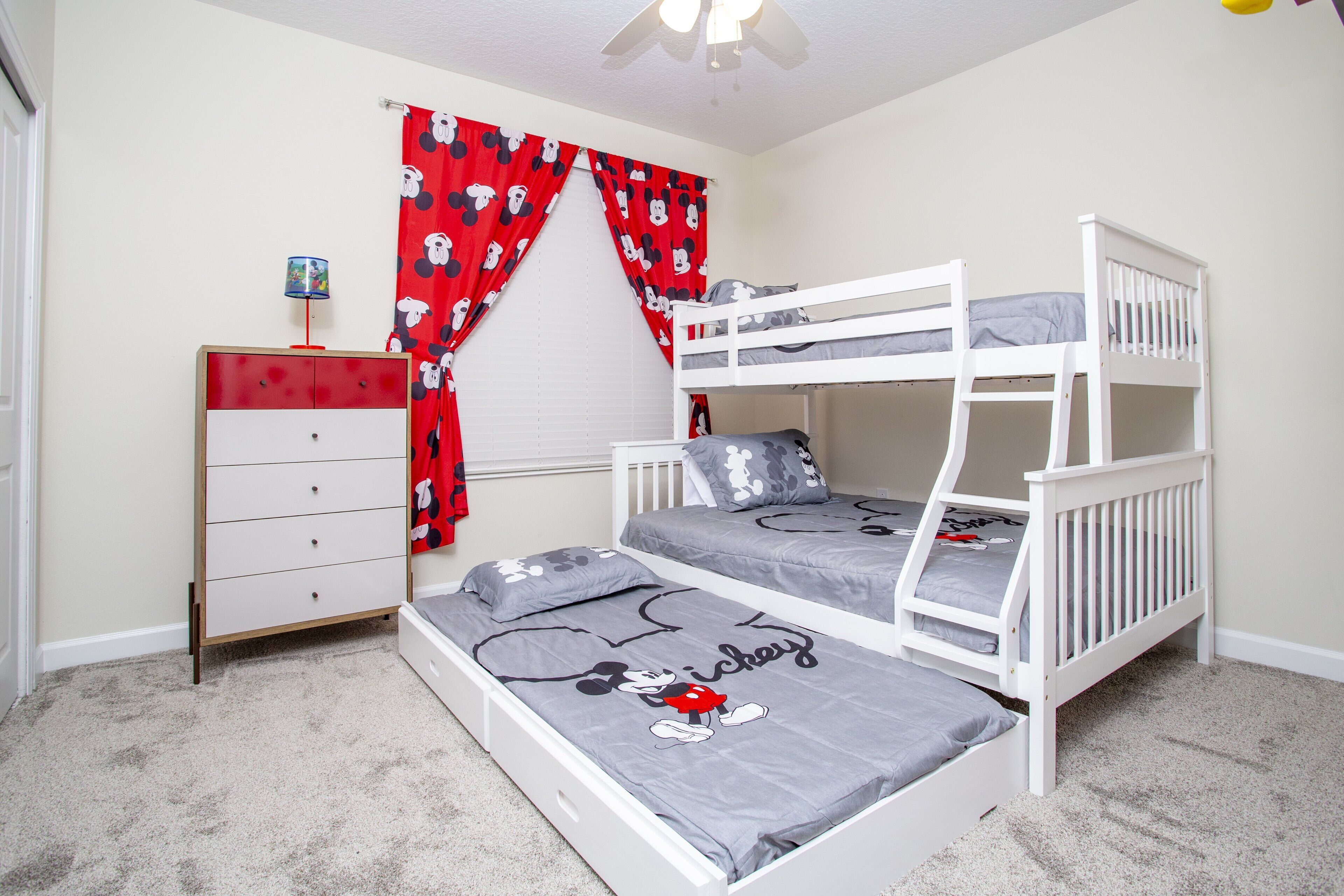 A bedroom with bunk beds, a dresser, and Mickey Mouse themed bedding.