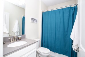A bathroom with a white sink, a toilet, a blue shower curtain, and a sign that reads "BATHROOM RULES & WASH - BRUSH - FLOSS - FLUSH". - Fabulous 5 Bedrooms Close to Disney at Champions Gate Resort 8988 (Kissimmee)