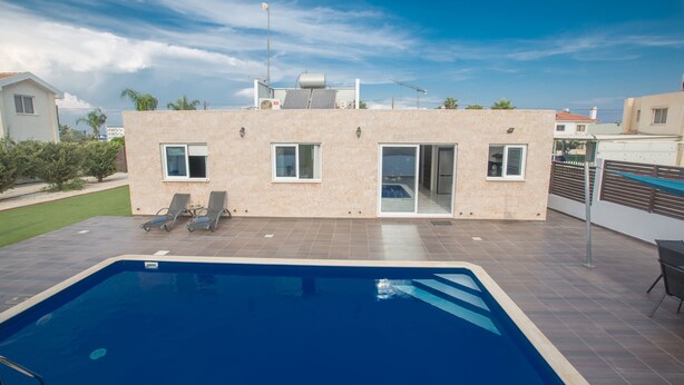 Une maison moderne dotée d’une piscine, d’un patio couvert et offrant une vue sur la mer.