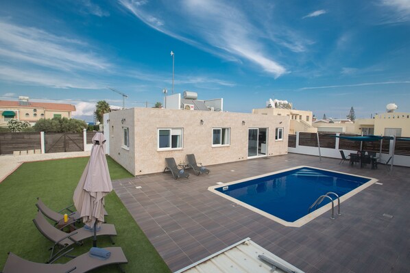 A rooftop pool area with a swimming pool, lounge chairs, and a small table with an umbrella.