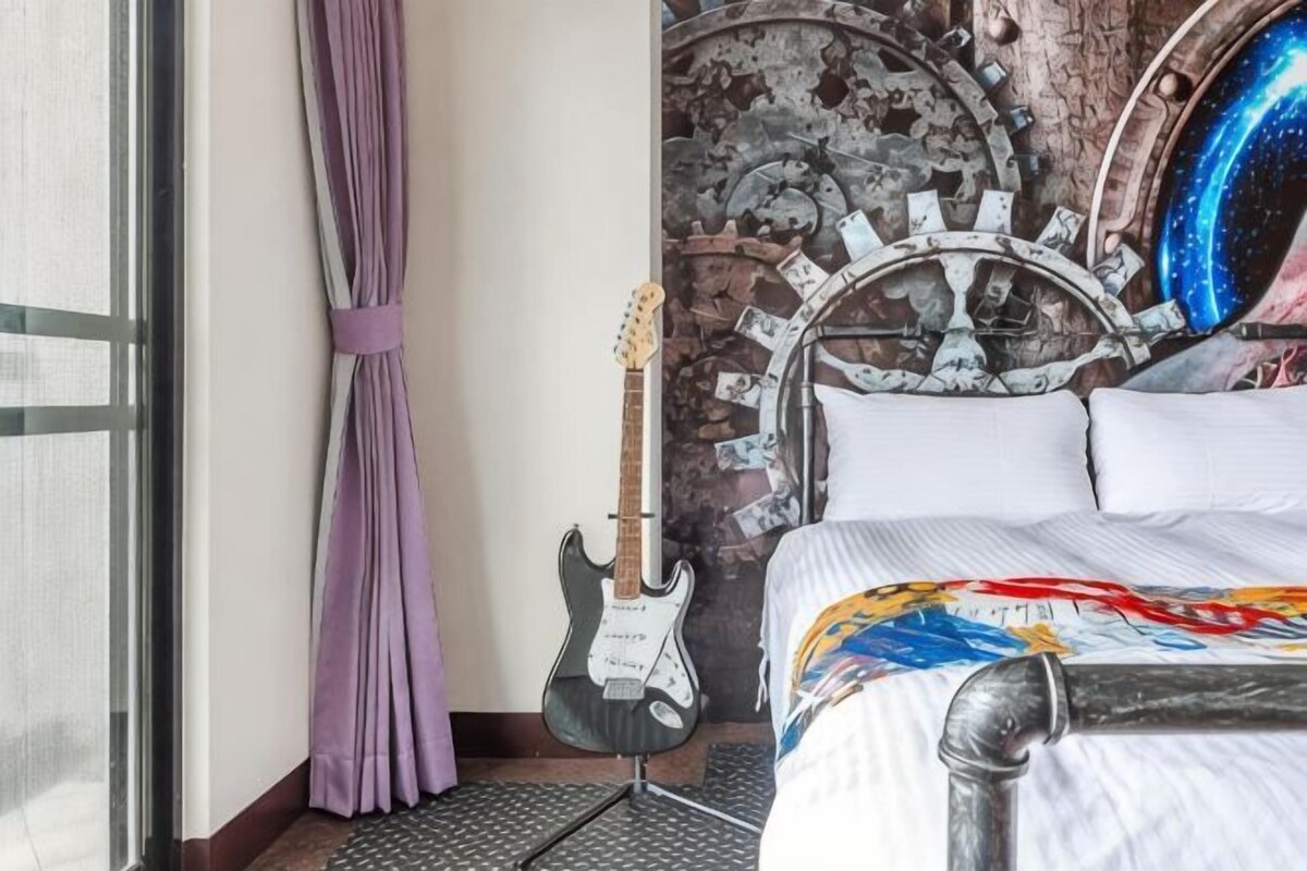 A room with a bed, a guitar, a curtain, and a wall with a nautical theme.