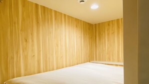 A room with wooden panel walls, a bed with white bedding, and a ceiling light. - bnb+ Osaka Shinsaibashi - Hostel (Osaka)