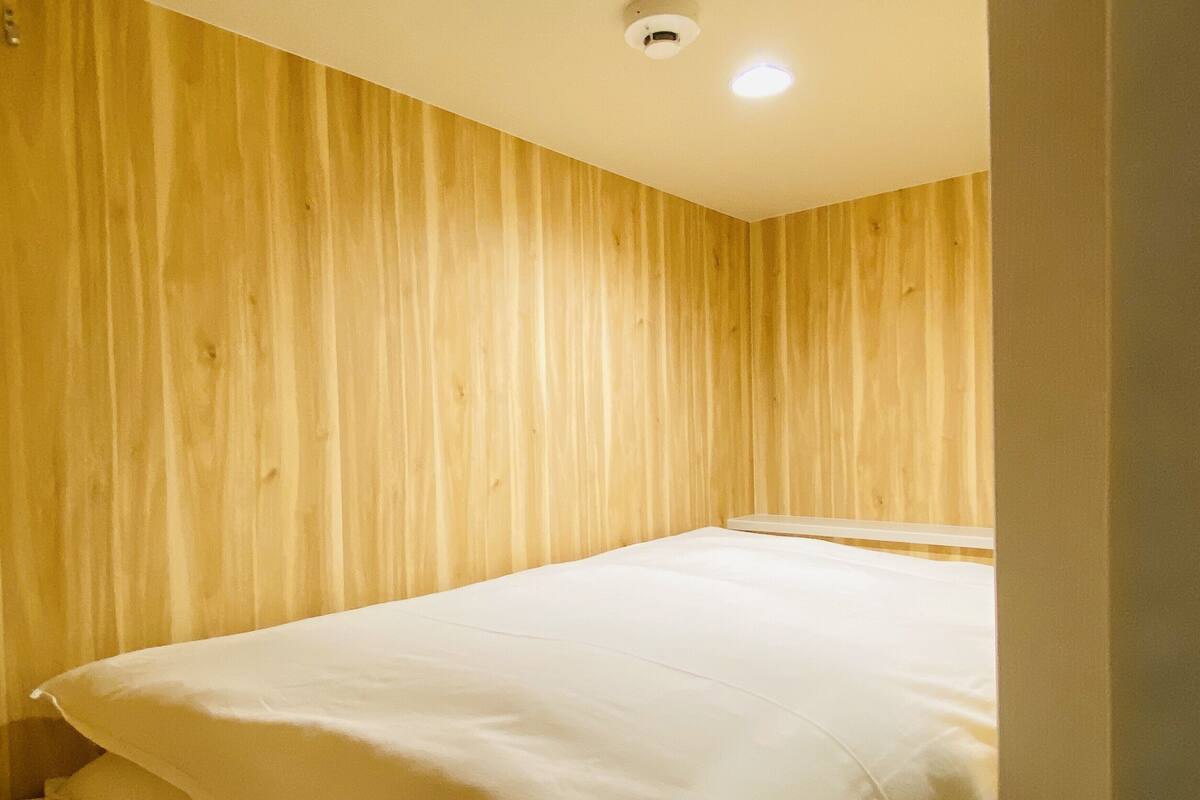 A room with wooden panel walls, a bed with white bedding, and a ceiling light.