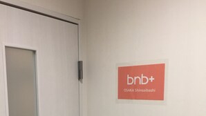 A door with a sign on the wall reading "bnb+" and "OSAKA SHINSAIBASHI". - bnb+ Osaka Shinsaibashi - Hostel (Osaka)
