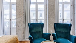 Une pièce avec deux fauteuils turquoise, une table basse en bois et un plaid à motifs sur un lit.