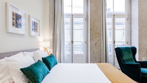Une chambre d’hôtel avec un lit, deux chaises, une lampe et une fenêtre avec des rideaux.