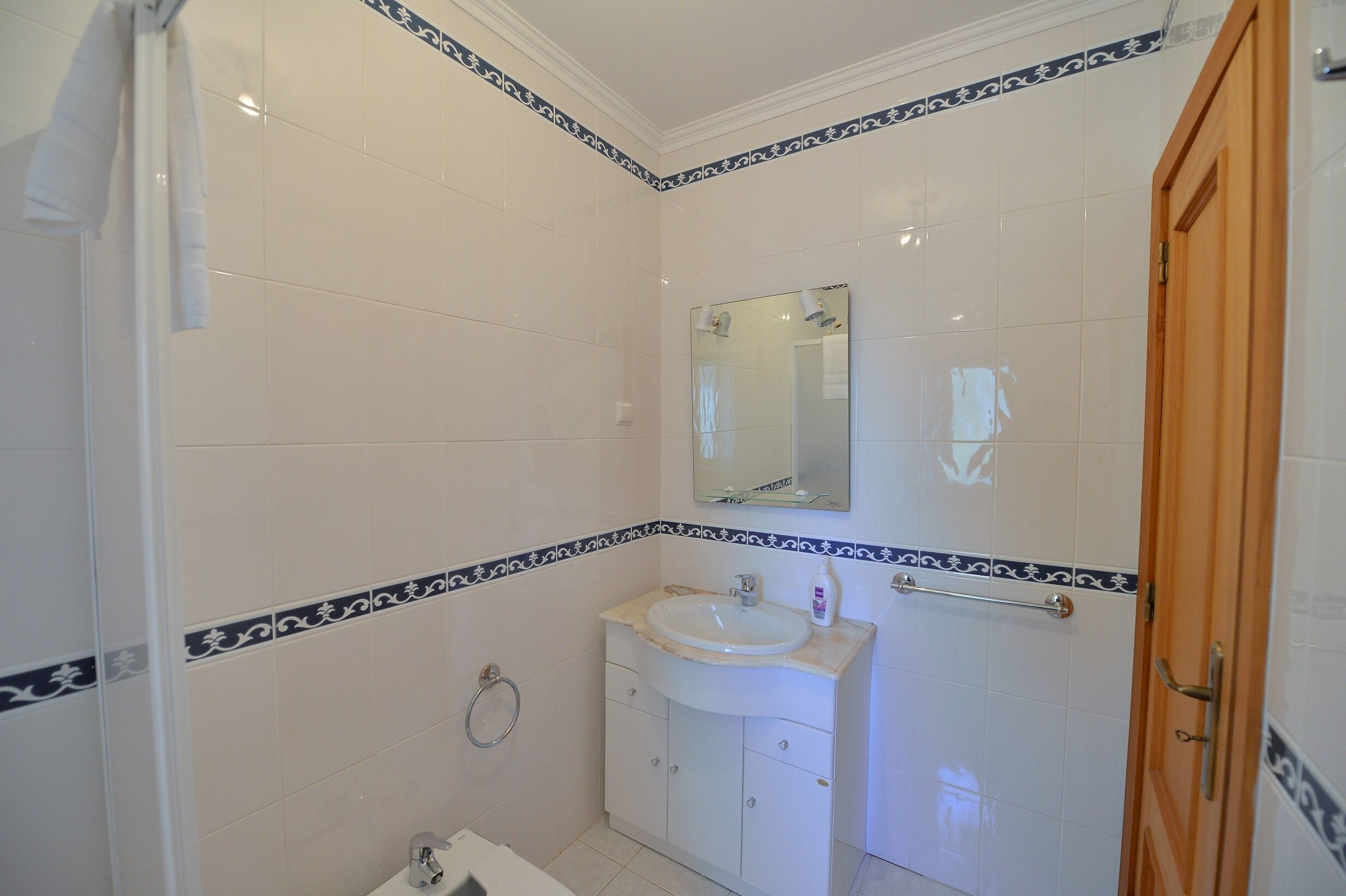A bathroom with white tiles, a sink, a mirror, and a wooden door.