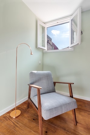Sit comfortably in the room with a chair against a light green wall, a floor lamp nearby, and a window offering a view of the outside.