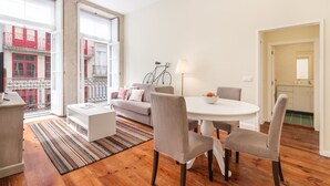 Een moderne woonkamer met een eethoek, een bank, een salontafel en uitzicht op een rood gebouw door een groot raam.
