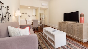 Een woonkamer met een bank, een televisie, een kast en een eethoek op de achtergrond.