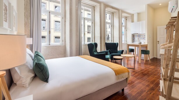 A hotel room with a large bed, two armchairs, a small table, and a wooden staircase. - Nada02 · Faisama #2 Studio Next to Ribeira (Porto)