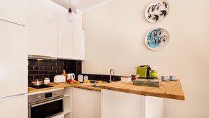 Une cuisine moderne avec des armoires blanches, un pare-feu noir et un plan de travail en bois. On y trouve une cuisinière, un four et divers ustensiles de cuisine sur le plan de travail.