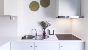 A modern kitchen with a stainless steel sink, a built-in stove, and two woven wall decorations. - Trind7 · Samasal Trindade Apartments #7 Garden View (Porto)