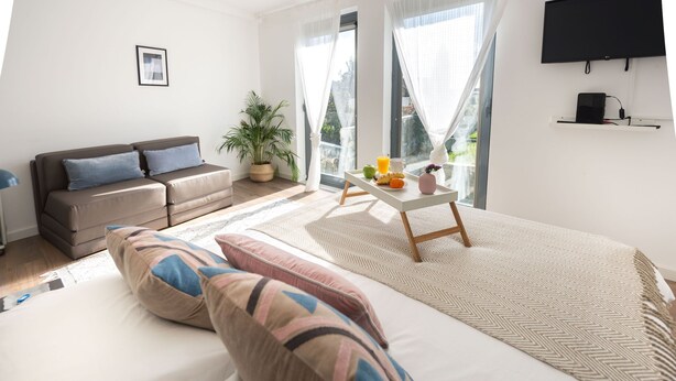 A modern hotel room with a large bed, a sofa, a dining table with breakfast, a TV, and a balcony with a plant. - Trind7 · Samasal Trindade Apartments #7 Garden View (Porto)