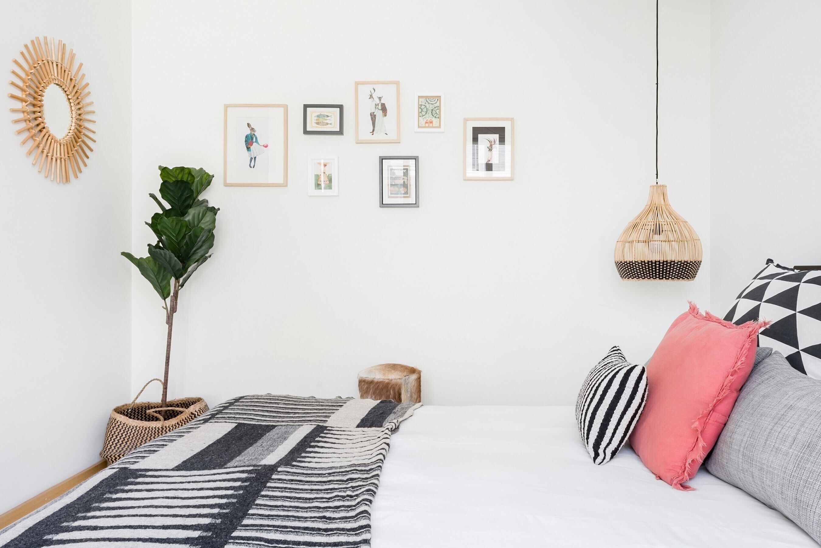 Un dormitorio ordenado con cama, almohadas, lámpara colgante y cuadros en la pared.
