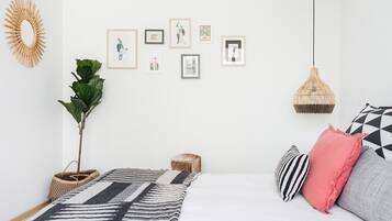 Un dormitorio ordenado con cama, almohadas, lámpara colgante y cuadros en la pared.