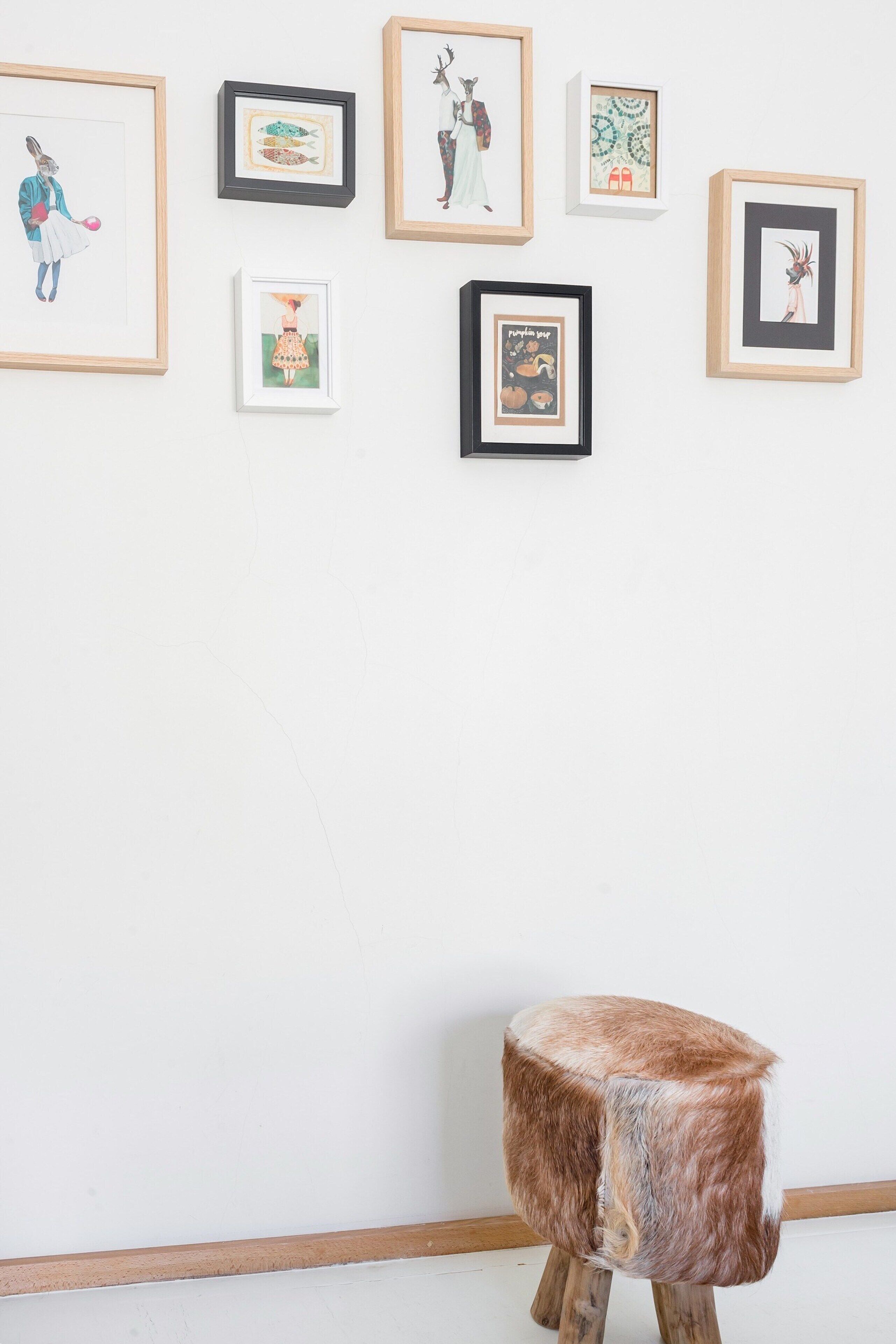 A gallery with framed artworks on the wall and a wooden stool in the foreground.