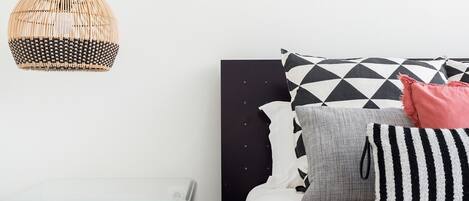 A modern bedroom with a glass bedside table, a black headboard, and a variety of pillows.