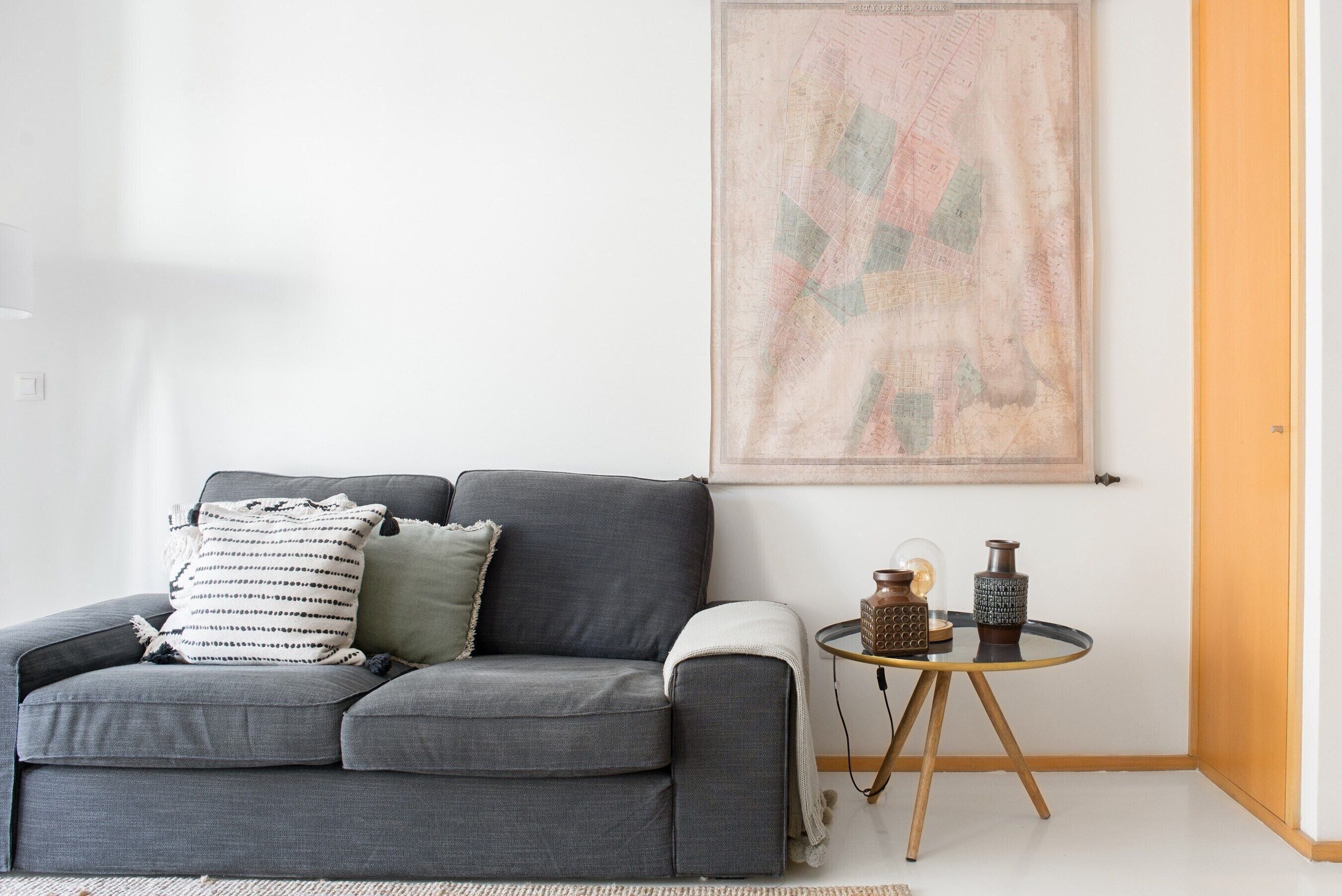 Een moderne woonkamer met een grijze bank, een kleine ronde tafel en een lijst met een abstract schilderij aan de muur.