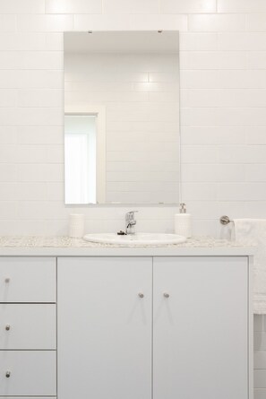 A bathroom with a white tiled wall, a large mirror, a white sink, and a cabinet with drawers. - Nada01 · Cute and Simple Apartment in the Historic District (Porto)