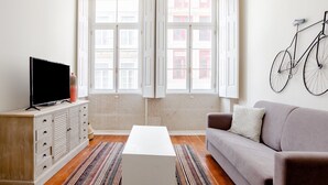 A living room with a television, a sofa, a coffee table, and a window with curtains. - Nada01 · Cute and Simple Apartment in the Historic District (Porto)
