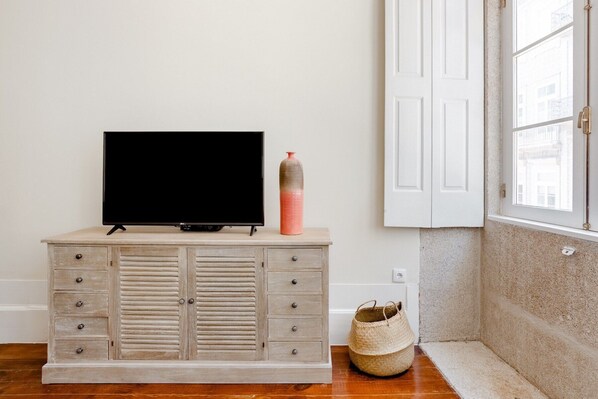 Ein Zimmer mit einem Holzkasten, einem Flachbildfernseher, einer Vase und einem gewebten Korb.