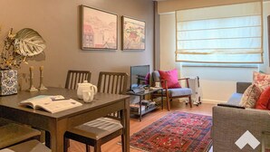 Ein Wohnzimmer mit Esstisch, Stühlen, einer Couch, einem Couchtisch, einem Fernseher und Kunstwerken an der Wand.