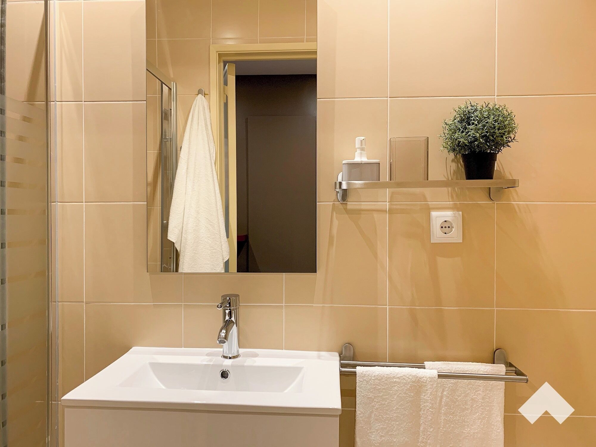 A bathroom with a white sink, a mirror, a towel rack, a potted plant, and a shelf with toiletries.