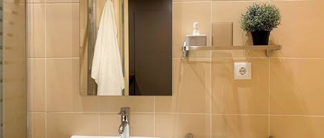 A bathroom with a white sink, a mirror, a towel rack, a potted plant, and a shelf with toiletries.