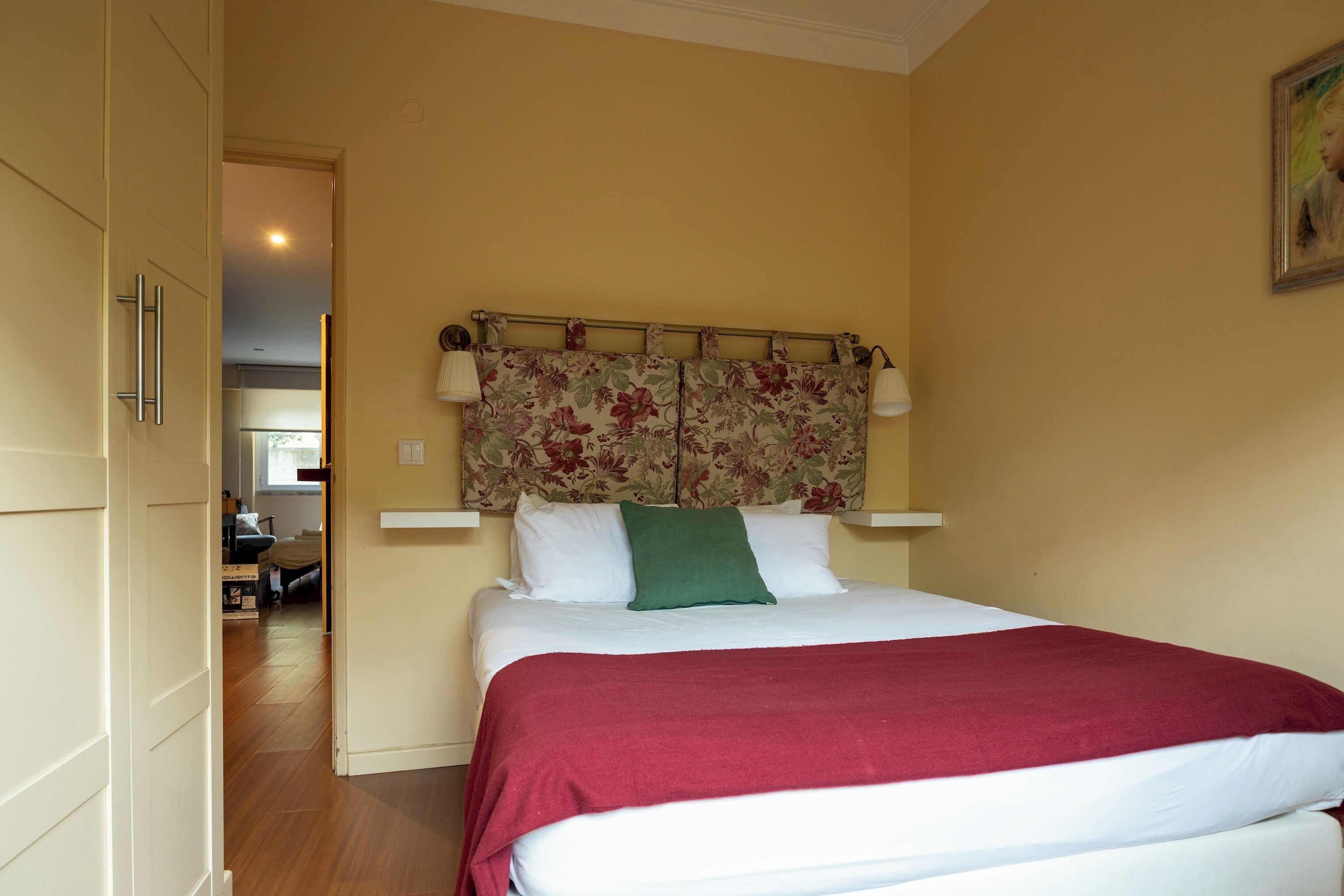 Un dormitorio con una cama, un cabecero estampado con motivos florales y una colcha roja.
