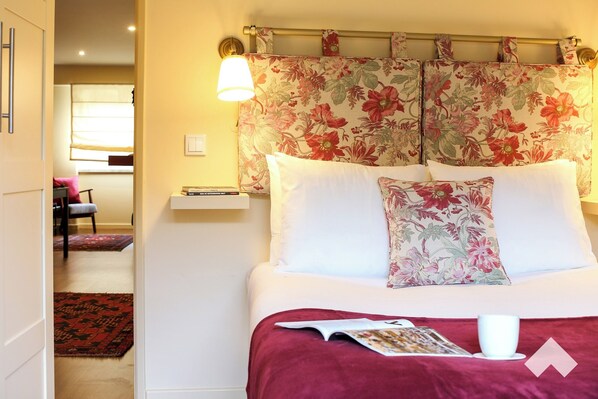 A neatly arranged bedroom with a bed, a bedside table, a nightstand, a floral headboard, and a window with curtains. - Graca1 · Apartment 92 · Your Home in Lisbon (Lisbon)