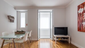 Ein zeitgemäßer Wohnbereich mit Essplatz, einem Fernseher auf einem Schrank und einem großen Fenster.