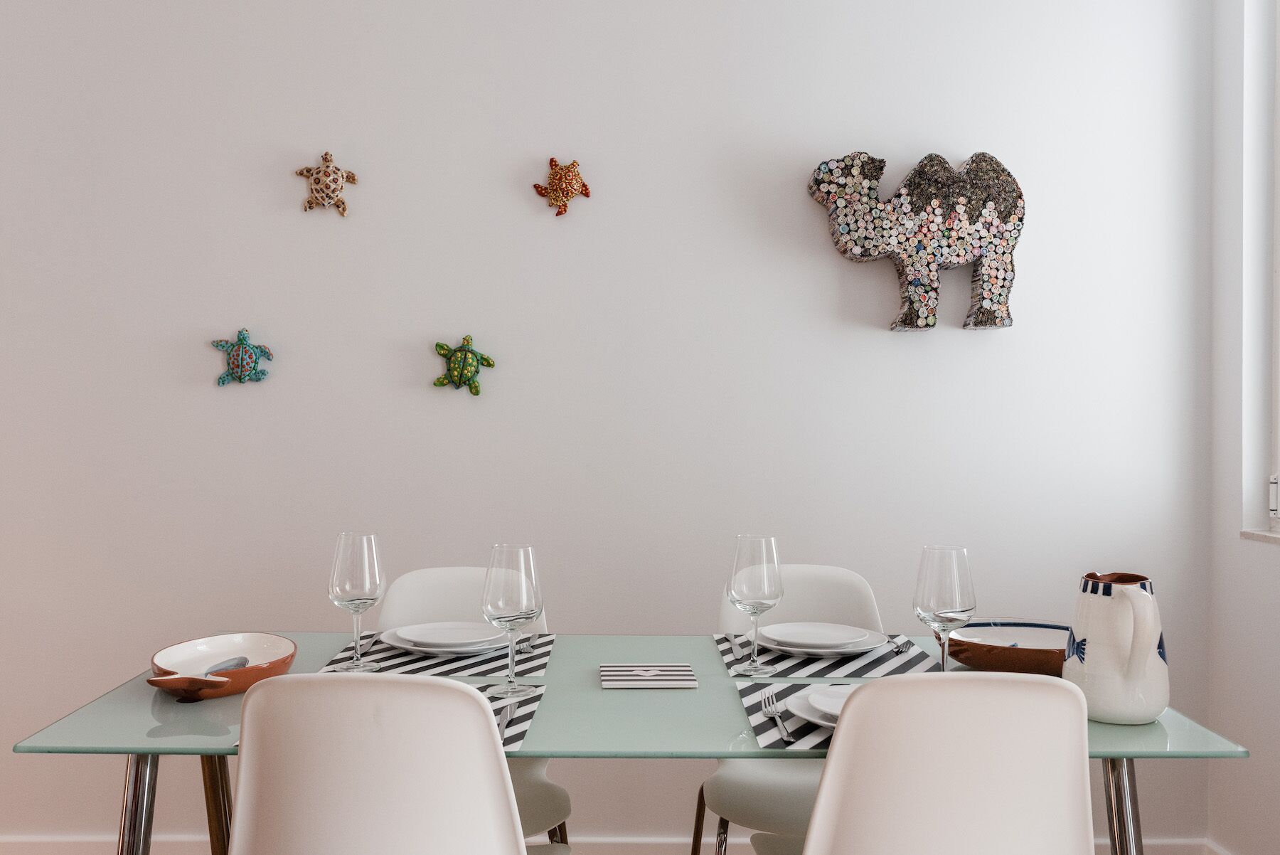 A dining area with a glass table set for four, white chairs, and decorative wall art.