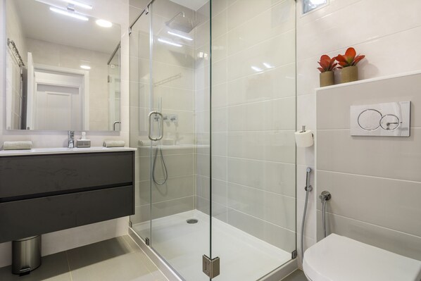 Une salle de bain moderne avec une douche à parois de verre, des toilettes et un meuble-lavabo avec un miroir.