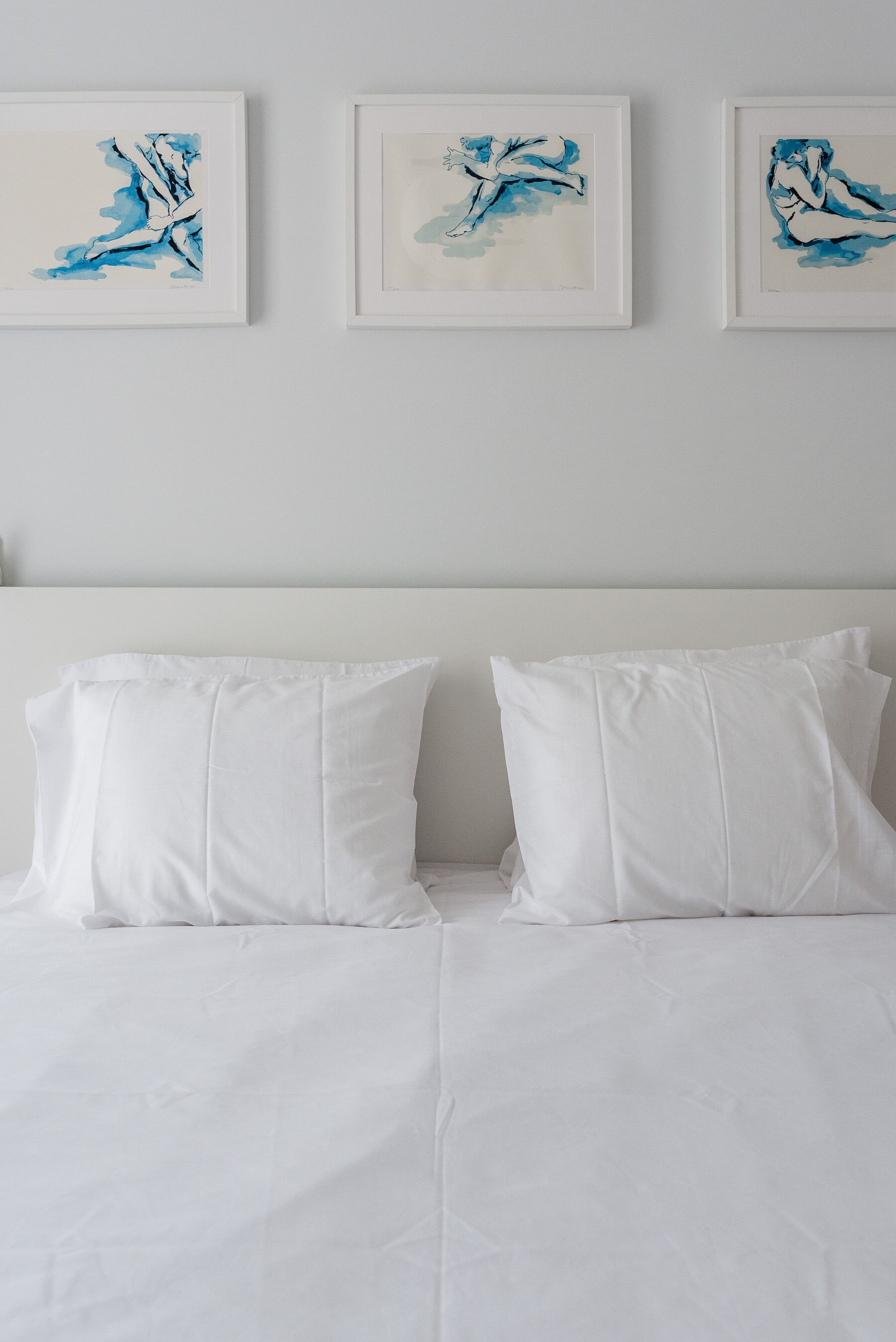 Una cama con ropa de cama blanca y dos almohadas, con tres cuadros enmarcados en la pared.
