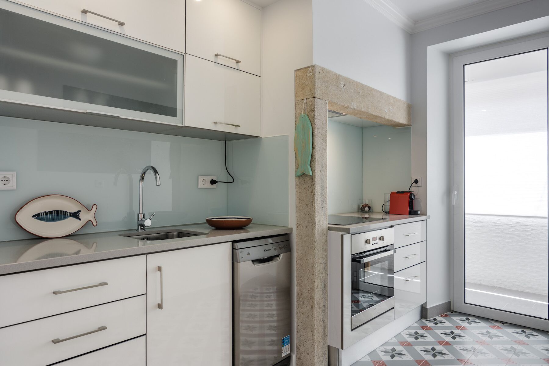 Una cocina moderna con armarios blancos, un lavavajillas de acero inoxidable y una cafetera roja.