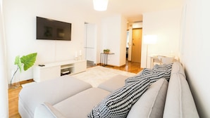 A modern hotel room with a large bed, a flat-screen TV mounted on the wall, a small side table, and a door leading to the bathroom.