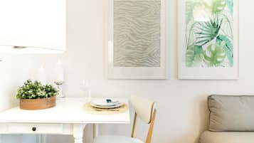 Een eetgedeelte met een witte tafel, een houten bijzettafeltje met kaarsen, en twee kunstwerken in lijsten aan de muur.