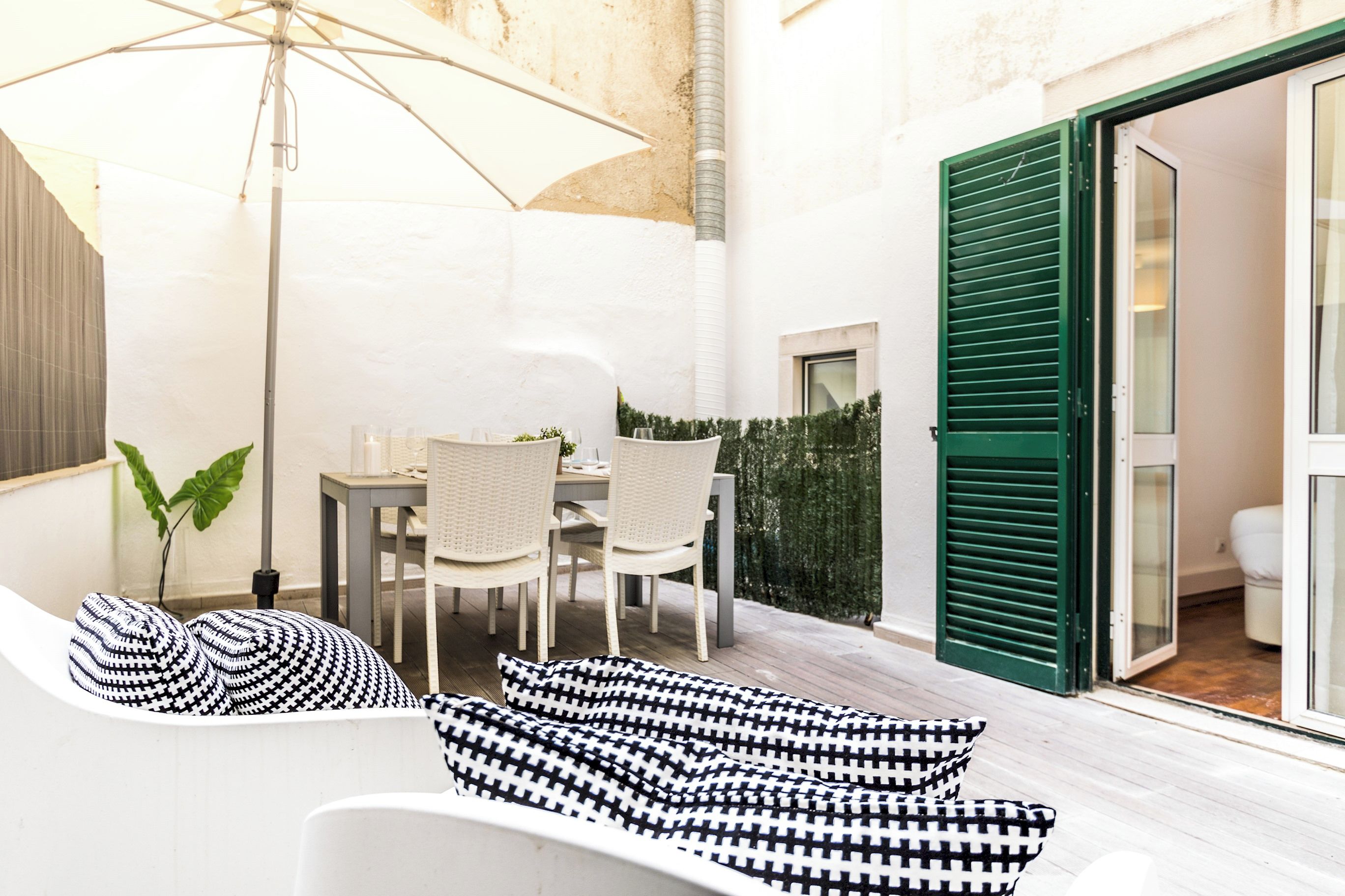 A modern outdoor seating area with a table and chairs, a large umbrella, and a sofa with patterned cushions.